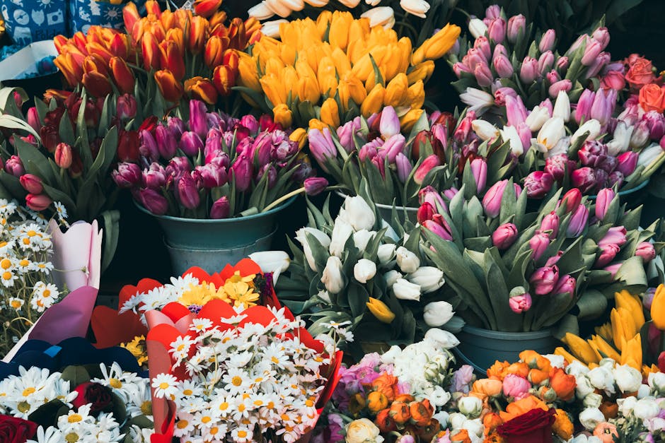 An abundant display of fresh flowers at a flower shop, featuring multiple bouquets and arrangements. Prominent among them are clusters of pink and white tulips, with some orange and yellow tulips arra