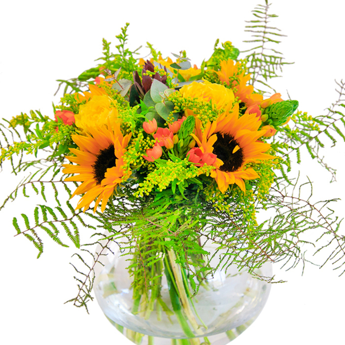 Bursting with the golden grace of Streatham's sunniest afternoons, this arresting bouquet is a tribute to all that is vivid and uplifting. Towering sunflowers stand proudly at the centre, their velvety brown cores surrounded by fresh petals in shades of luminous yellow and orange. Paired elegantly are yellow roses, each layered bloom carefully coaxed open to reveal intricate spirals in soft buttery tones. Dotted artfully between the larger blooms, red Hypericum berries sparkle, drawing the eye like glints of laughter amidst the greenery. Cascading fern fronds and sprigs of goldenrod give the arrangement layers of movement and texture, their greens reminiscent of the lush lawns in Streatham's parks. The glass bowl vase, pure in its simplicity, reveals the vibrant stems crisscrossing within, the water glistening beneath as sunlight might on the ponds of The Rookery. Gentle notes of eucalyptus and feathery filler blend together, softening the bouquet's lines and evoking the calming hush of a summer breeze. This arrangement, handcrafted by our experienced Streatham Florist, is perfect for marking joyful occasions or sending a bright wave of cheer to neighbours and loved ones across the SW16 community.