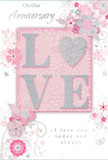 The image presents a beautifully styled anniversary card that celebrates enduring romance through a soft palette of pastel pinks, silvery greys, and delicate whites. At its centre, the word LOVE is boldly featured in raised, glittered lettering, with a subtle sparkle that catches the light like fine stardust. The letters are substantial enough to be clearly felt by touch, and the glitter edging adds both visual drama and a sense of occasion. Within the word, the letter O is transformed into a shimmering silver heart, slightly textured and more metallic in tone, becoming a small jewel-like focal point. Surrounding this central word, fluid sprays of illustrated blooms in blush and mauve drift outward, their watercolor-soft petals and graceful stems echoing the romantic curves of English garden flowers-a style often echoed in anniversary arrangements delivered around Streatham and nearby residential streets. Fine, swirling lines weave between the blossoms, accompanied by tiny petals, curls, and a few almost-hidden butterflies, suggesting movement and gentle whimsy. The background remains a calm, powder-pink field, allowing the silver accents and floral details to emerge without distraction. Scripted text, including phrases such as On Our Anniversary and I love you today and always, appears in an understated yet expressive calligraphy, harmonising with the card's flowing decorative lines. Overall, the composition conveys a hushed, heartfelt intimacy-the visual equivalent of a softly spoken promise shared over dinner while a fresh bouquet rests in a vase nearby.